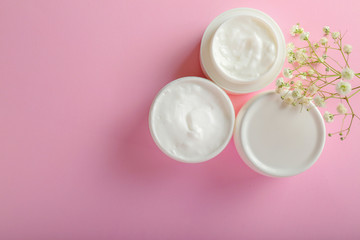 Jars of body cream on color background