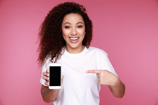 Portrait of a happy young african girl showing plastic credit card while holding mobile phone isolated over yellow background