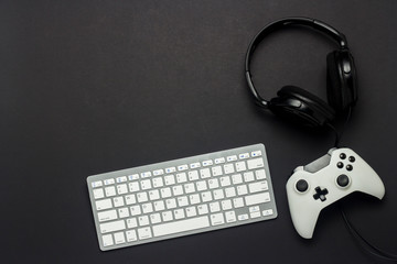 Keyboard, gamepad and headphones on a black background. The concept of the game on the console,...