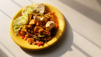 Papaya salad with sweet corn and salted egg in yellow dish on table in sunlight and have space for write wording, very popular fusion Thai north eastern street food for fat people and general tourist