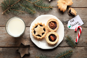 Plate with tasty mince pies and glass of milk on wooden table