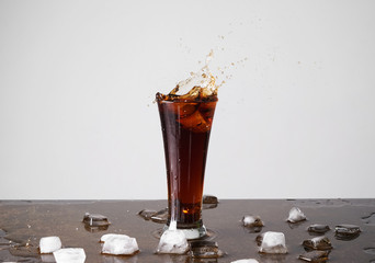 Glass of splashing cola on table against light background