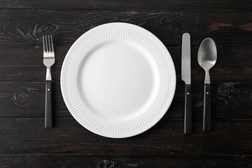 Empty ceramic plate with cutlery on dark wooden background