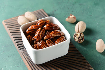 Bowl with tasty candied pecan nuts on color table