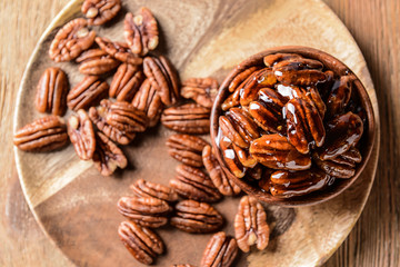 Bowl and plate with tasty pecan nuts on wooden table