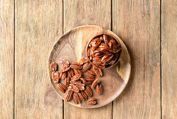 Bowl and plate with tasty pecan nuts on wooden table