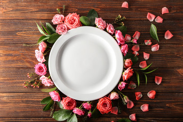 Clean empty plate and flowers on wooden background