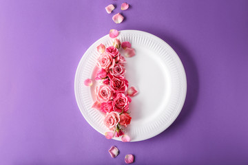 Plate with beautiful flowers on color background