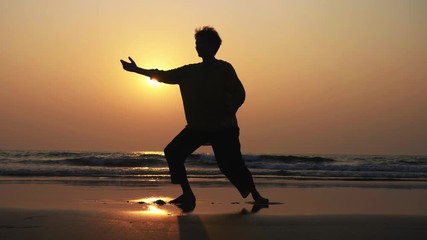 Silhouette of active senior woman practicing tai chi gymnastic on sandy beach. - Powered by Adobe