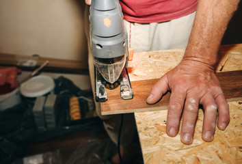 Worker is holding in hands power jigsaw and cutting laminate flooring in apartment. Maintenance repair works renovation in the flat with scroll saw. Restoration of wooden parquet floor planks indoors.