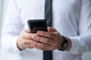 Closeup of business man browsing on smartphone. Entrepreneur holding digital device. Communication and technology concept. Cropped front view.