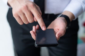 Closeup of business man tapping on smartphone screen. Entrepreneur holding and using digital device. Communication and technologies in business concept. Cropped front view.