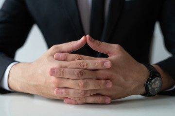 Obraz premium Closeup of pensive entrepreneur with clasped hands. Business man wearing suit and watch. Contemplation or waiting concept. Cropped front view.