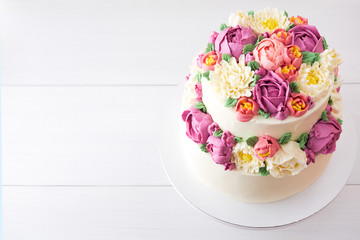 Two-tiered white wedding cake decorated with color cream flowers on a white wooden background. Top view.