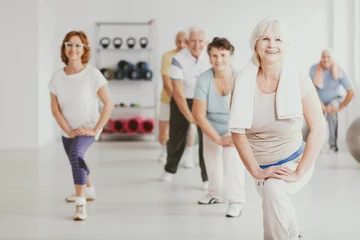 Foto op Canvas Smiling senior woman exercising with group of active seniors in fitness center © Photographee.eu
