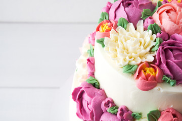 Two-tiered white wedding cake decorated with color cream flowers on a white wooden background.