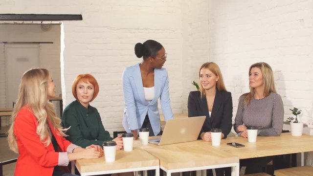 Happy African business woman, group leader celebrating success with female members of her team, being overjoyed, clapping hands with the others at meeting.
