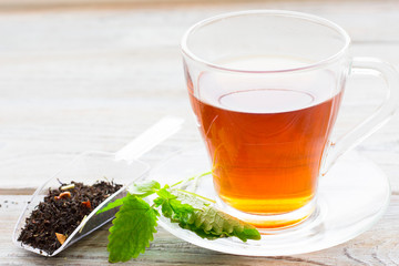Black tea ceremony - glass full of tea, tea leaves, spices on a wooden boards background