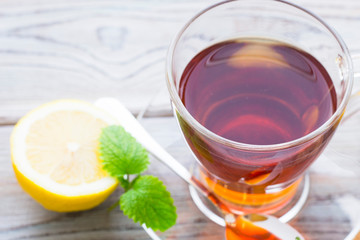 Black tea ceremony - glass full of tea, sugar, yellow lemon, tea leaves, spices on a wooden boards background