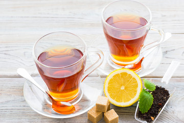 Black tea ceremony - glass full of tea, sugar, yellow lemon, tea leaves, spices on a wooden boards background