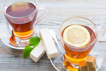 Black tea ceremony - glass full of tea, sugar, yellow lemon, tea leaves, spices on a wooden boards background