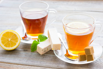 Black tea ceremony - glass full of tea, sugar, yellow lemon, tea leaves, spices on a wooden boards background