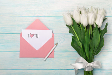 A bouquet of white tulips with love note and color envelope on blue wooden boards