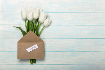 A bouquet of white tulips with a love note and envelope on blue wooden boards