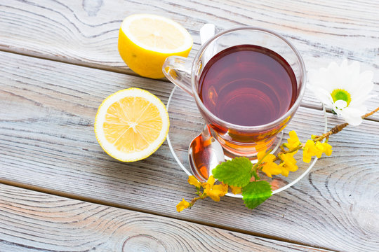 Black tea ceremony - glass full of tea, sugar, yellow lemon, tea leaves, spices on a wooden boards background
