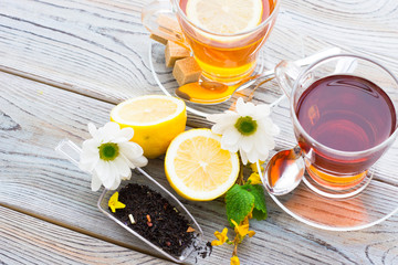 Black tea ceremony - glass full of tea, sugar, yellow lemon, tea leaves, spices on a wooden boards background