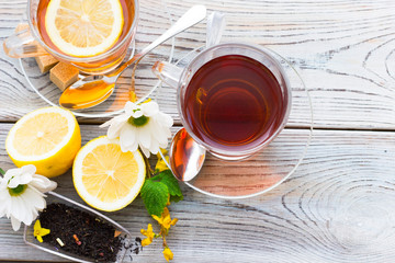 Black tea ceremony - glass full of tea, sugar, yellow lemon, tea leaves, spices on a wooden boards background