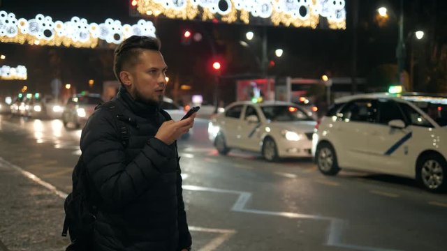 Young hipster guy using modern smartphone outdoors, man chatting with friends at social networks while walking at evening city streets use audio message voice recognition cars center