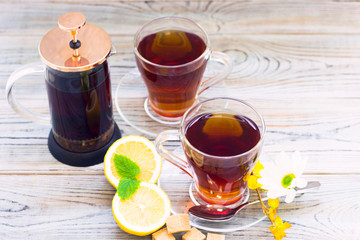 Black tea ceremony - glass full of tea, glass pot, sugar, yellow lemon, flower, tea leaves, spices on a wooden boards background