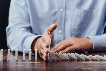 partial view of man preventing dominoes from falling on desk