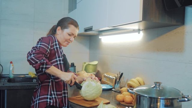 woman in the kitchen preparing a meal concept. girl in the kitchen cuts cabbage with a knife. cook vegetarian food healthy food. girl at home in lifestyle the kitchen slow motion video