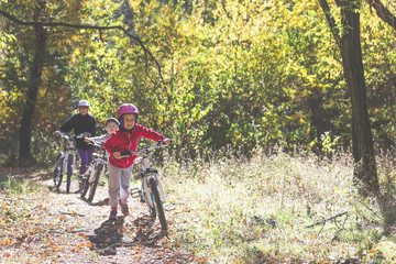 Mother and two daughters with bikes go uphill in the autumn forest.