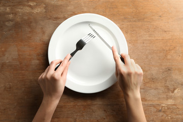 Female hands with cutlery and empty plate on wooden background