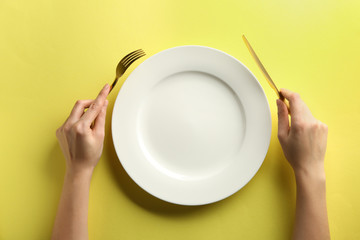 Female hands with cutlery and empty plate on color background
