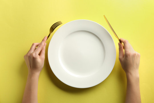 Female hands with cutlery and empty plate on color background