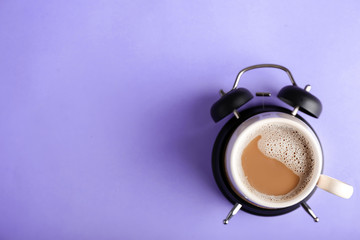 Cup of coffee and alarm clock on color background