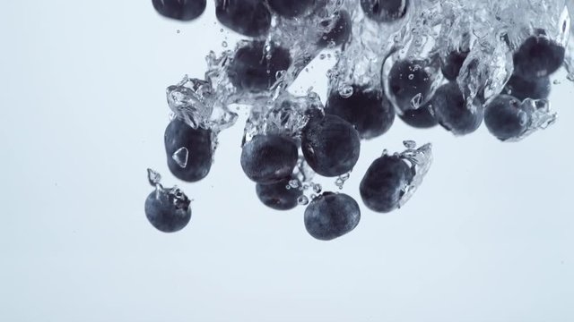 Slow motion shot of blueberries splashing into water