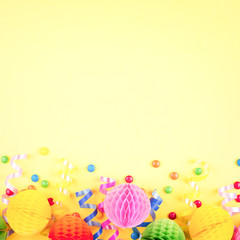 Obraz premium Birthday party background on yellow. Top view. Border made of colorful serpentine, balls and candies.