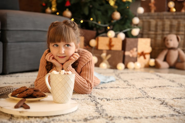 Cute little girl with hot chocolate and cookies at home on Christmas eve