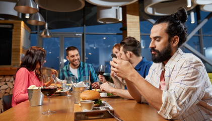technology, lifestyle and people concept - man dining with friends and messaging on smartphone at restaurant