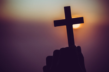 concept of religion. Silhouette of a man praying with a cross in hand at sunrise.