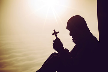 concept of religion. Silhouette of a man praying with a cross in hand at sunrise.