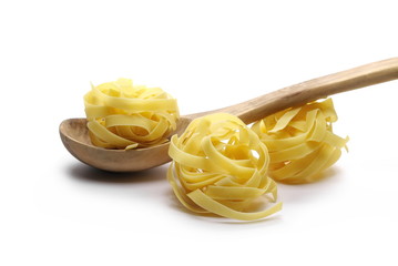 Raw tagliatelle pasta noodles with wooden spoon isolated on white background