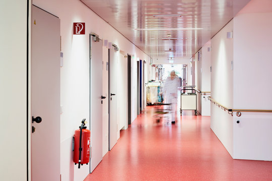 Krankenhaus mit Korridor Feuerl&ouml;scher und Mann mit Rollator unscharf in Zentralperspektive