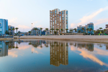 Reflexiones sobre el agua al atardecer. En una playa a al caer el dia sobre edificios de verano en la playa de San Juan, Alicante España