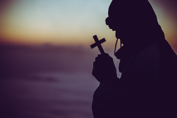 concept of religion. Silhouette of a man praying with a cross in hand at sunrise.